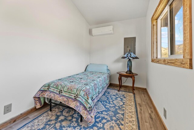 bedroom with an AC wall unit, electric panel, baseboards, and wood finished floors