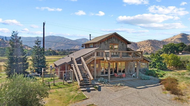 rear view of house featuring a deck with mountain view, a patio area, stairs, and fence