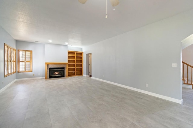 unfurnished living room with a fireplace with flush hearth, ceiling fan, baseboards, and stairs