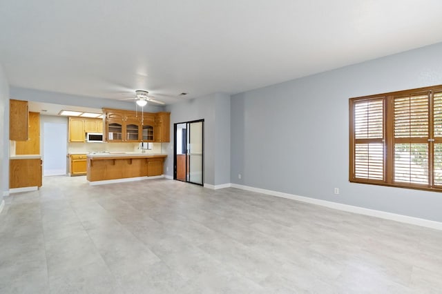 unfurnished living room with ceiling fan and baseboards