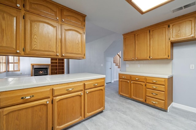 kitchen featuring a lit fireplace, brown cabinetry, visible vents, and baseboards