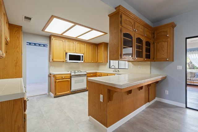 kitchen with a peninsula, white appliances, a skylight, a sink, and visible vents