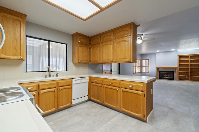 kitchen with brown cabinetry, open floor plan, white dishwasher, a peninsula, and a lit fireplace