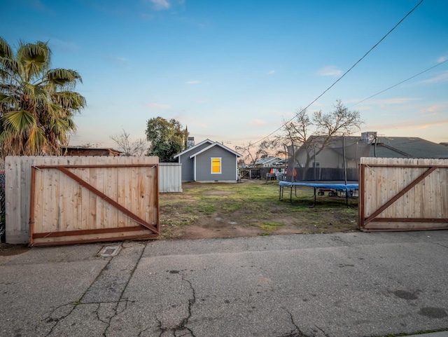 yard at dusk featuring a trampoline, a gate, and fence