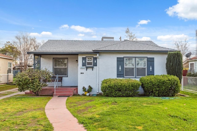 bungalow-style home with stucco siding, a shingled roof, covered porch, a front yard, and fence