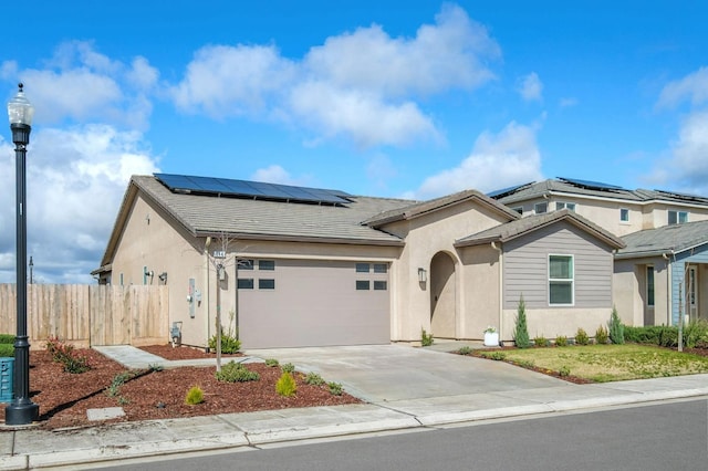 view of front of home featuring concrete driveway, an attached garage, fence, roof mounted solar panels, and stucco siding