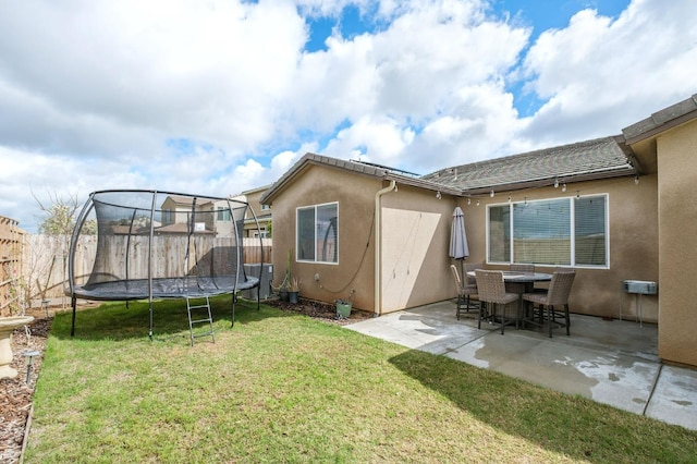 back of house featuring fence, a yard, stucco siding, a trampoline, and a patio area