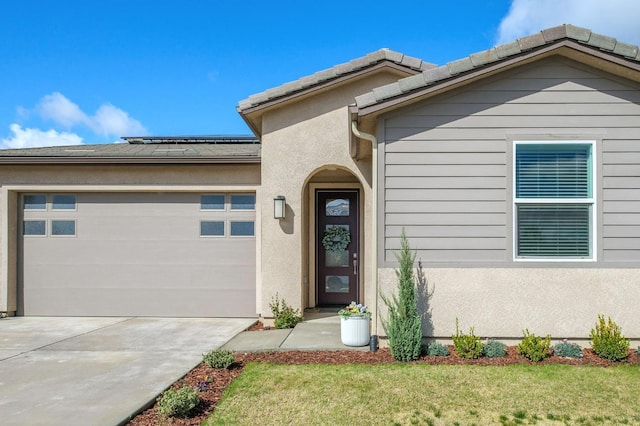 entrance to property with a yard, solar panels, stucco siding, a garage, and driveway