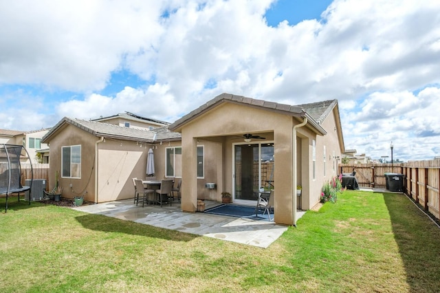 rear view of property with a trampoline, a patio, central air condition unit, stucco siding, and a fenced backyard