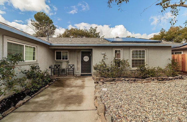 view of front facade with roof mounted solar panels, fence, and stucco siding