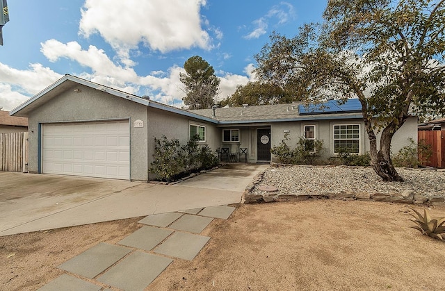 ranch-style home featuring solar panels, stucco siding, concrete driveway, fence, and a garage