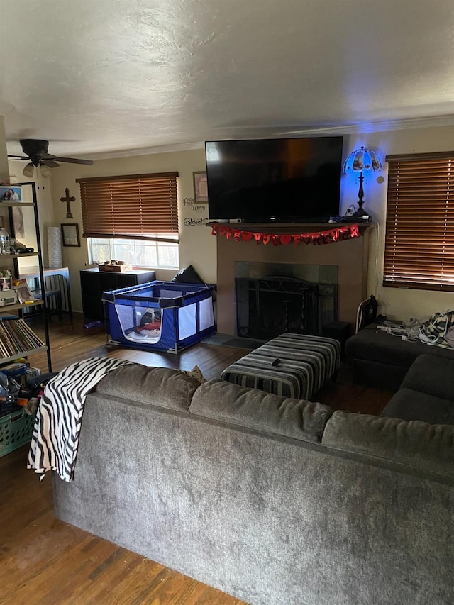 living area featuring a fireplace, a ceiling fan, wood finished floors, and ornamental molding