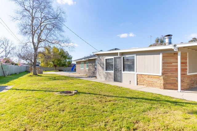 rear view of house with a yard, stone siding, and fence