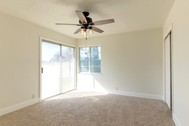 carpeted spare room with a ceiling fan and baseboards