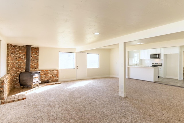 unfurnished living room with light carpet, a sink, a wood stove, and baseboards