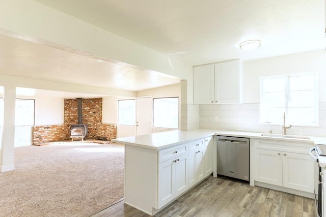 kitchen with a peninsula, a wood stove, stainless steel dishwasher, white cabinetry, and a sink