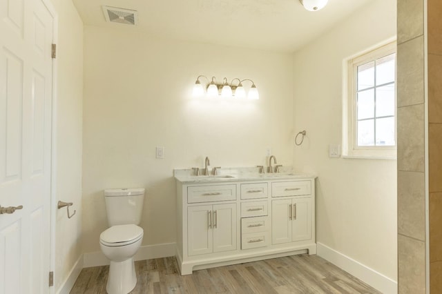 bathroom featuring toilet, visible vents, a sink, and wood finished floors