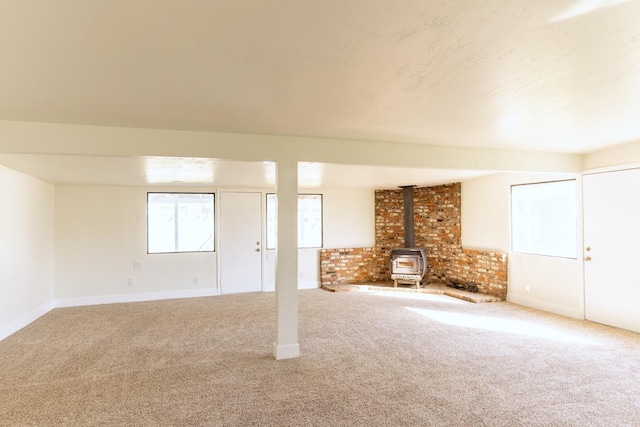 below grade area with carpet floors, a wood stove, and baseboards