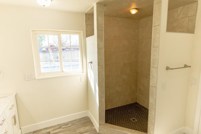 bathroom with wood finished floors, a tile shower, vanity, and baseboards