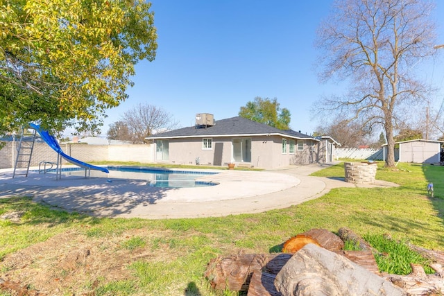 rear view of property featuring an outbuilding, a playground, stucco siding, a lawn, and fence