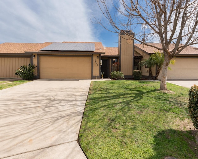 view of front of house featuring an attached garage, solar panels, concrete driveway, a chimney, and a front yard