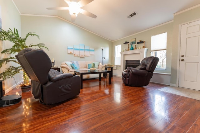 living area with a fireplace, lofted ceiling, visible vents, ornamental molding, and wood finished floors