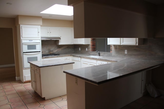 kitchen with a skylight, white double oven, a peninsula, under cabinet range hood, and a sink