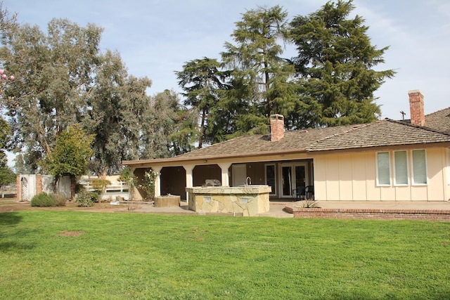 back of property with board and batten siding, a patio area, a chimney, and a lawn