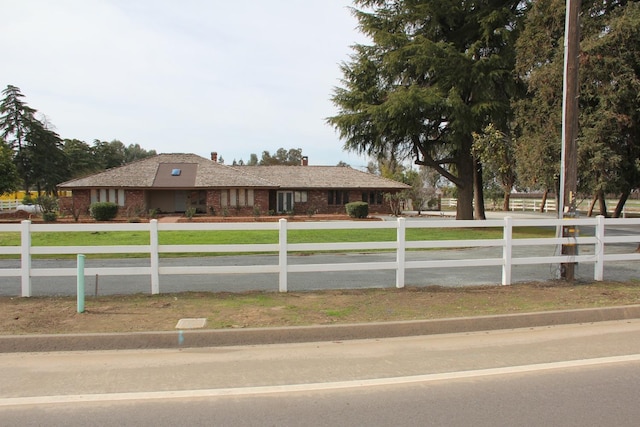 ranch-style home featuring a fenced front yard, a chimney, a front lawn, and brick siding