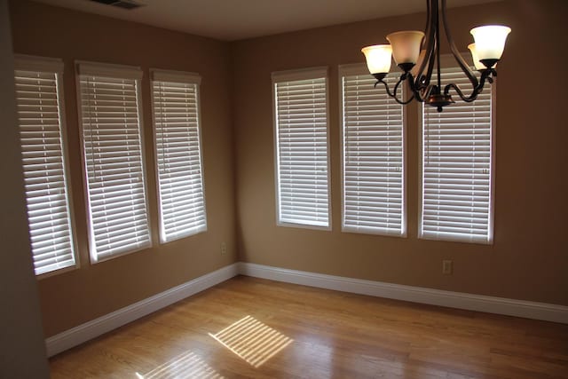 unfurnished dining area featuring baseboards, visible vents, a chandelier, and wood finished floors