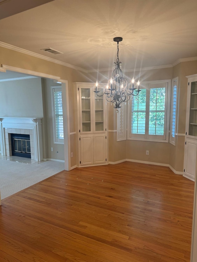 unfurnished dining area with a tile fireplace, light wood-style flooring, and crown molding