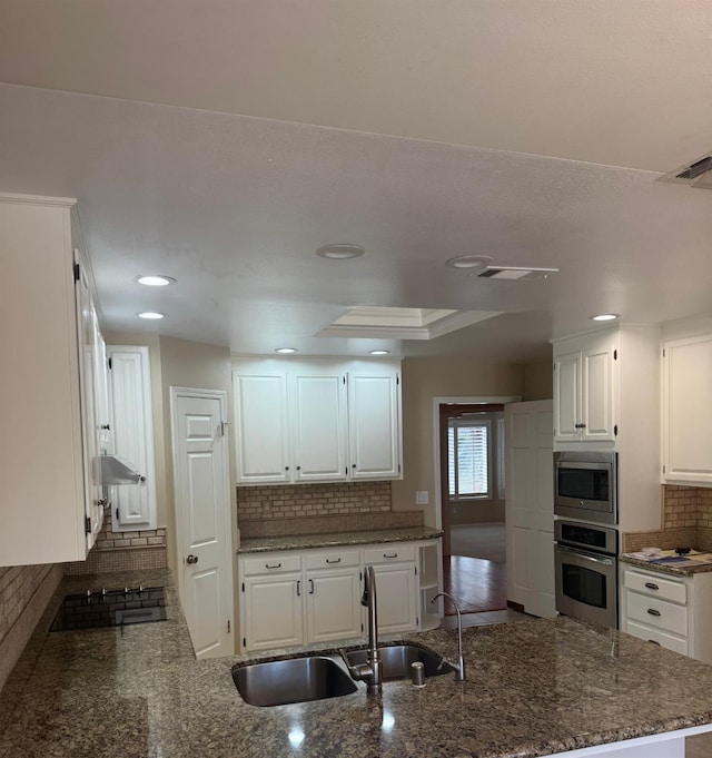 kitchen featuring stainless steel appliances, a peninsula, a sink, visible vents, and white cabinets