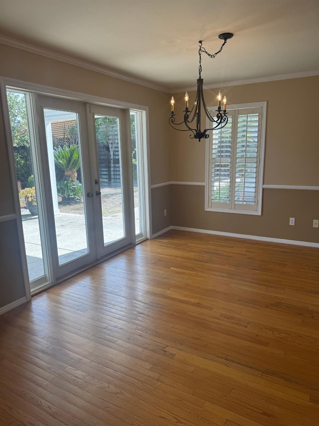 empty room featuring french doors, ornamental molding, wood finished floors, a chandelier, and baseboards