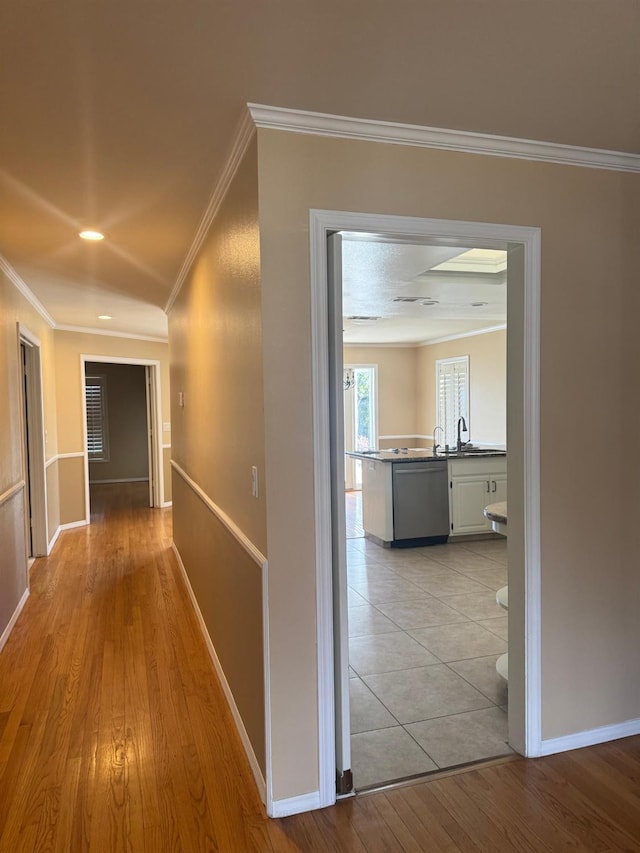 corridor featuring baseboards, ornamental molding, a sink, and light wood-style floors