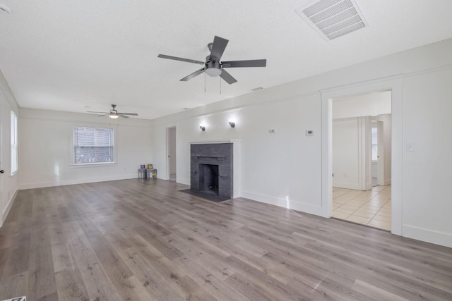 unfurnished living room with ceiling fan, wood finished floors, a fireplace with flush hearth, and visible vents