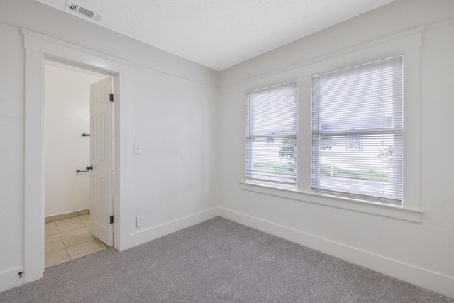 tiled spare room with a textured ceiling, carpet floors, visible vents, and baseboards