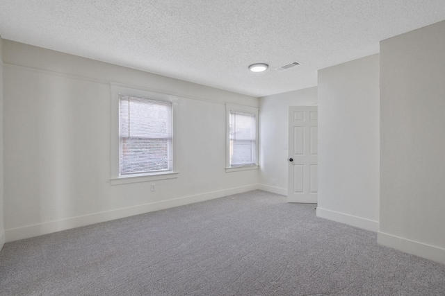 carpeted empty room featuring a textured ceiling, visible vents, and baseboards