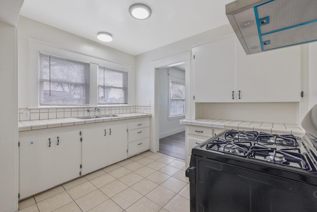 kitchen with black gas range oven, light tile patterned floors, white cabinets, and a sink