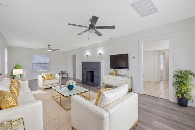 living area featuring light wood-style flooring, visible vents, ceiling fan, and a fireplace with flush hearth