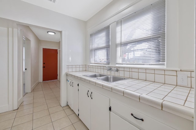 kitchen featuring tile countertops, light tile patterned floors, white cabinets, and a sink