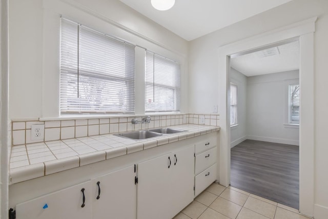 kitchen with light tile patterned flooring, a sink, white cabinets, and a healthy amount of sunlight