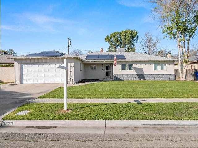 single story home featuring brick siding, concrete driveway, an attached garage, a front yard, and roof mounted solar panels