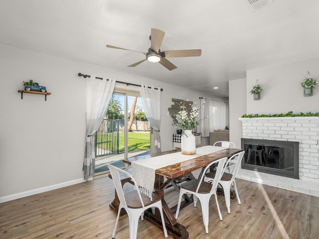 dining area with light wood-type flooring, a brick fireplace, ceiling fan, and baseboards