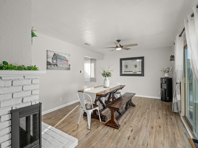 dining area featuring visible vents, a brick fireplace, light wood-style flooring, and baseboards