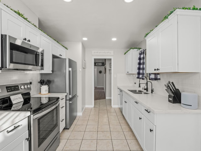 kitchen with appliances with stainless steel finishes, a sink, white cabinetry, backsplash, and light tile patterned flooring