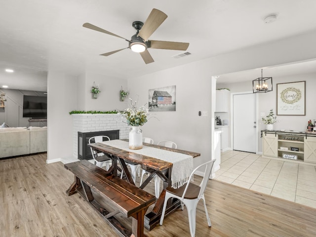 dining space with light wood finished floors, baseboards, visible vents, a ceiling fan, and a fireplace