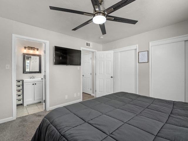 bedroom featuring multiple closets, light carpet, connected bathroom, a sink, and baseboards