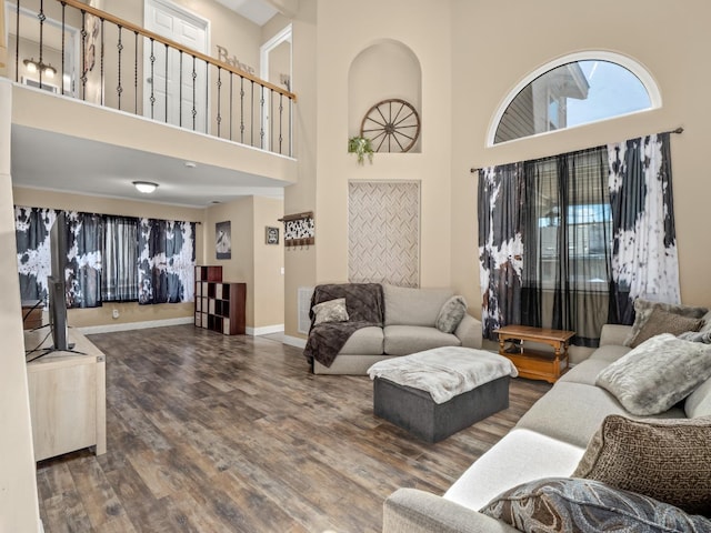 living area featuring a towering ceiling, baseboards, and wood finished floors