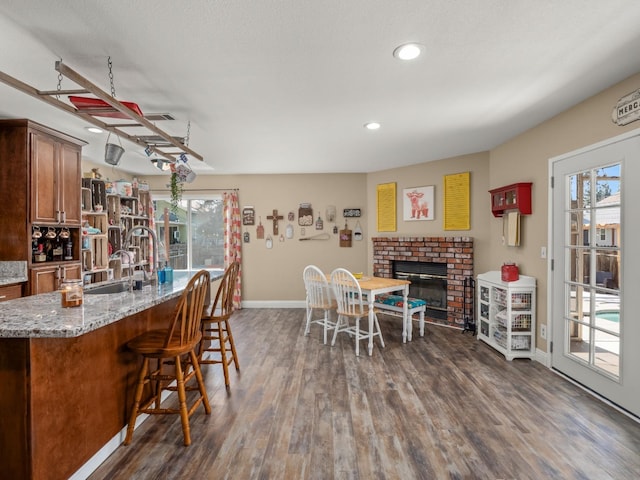 dining room with dark wood-style flooring, a brick fireplace, a wealth of natural light, and baseboards