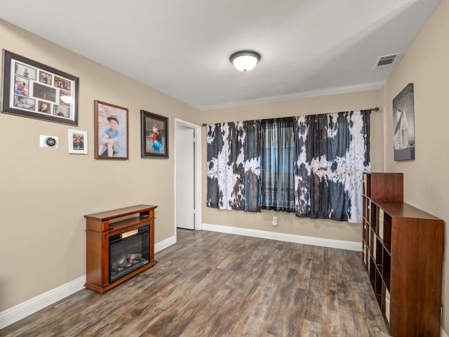 interior space featuring wood finished floors, a glass covered fireplace, visible vents, and baseboards